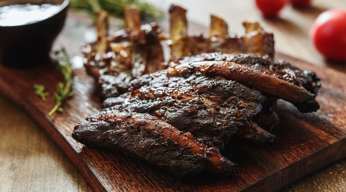 BBQ grilled pork ribs in Barbecue sauce on vintage wooden table background. There are several small fresh red tomatoes on a blurred background.