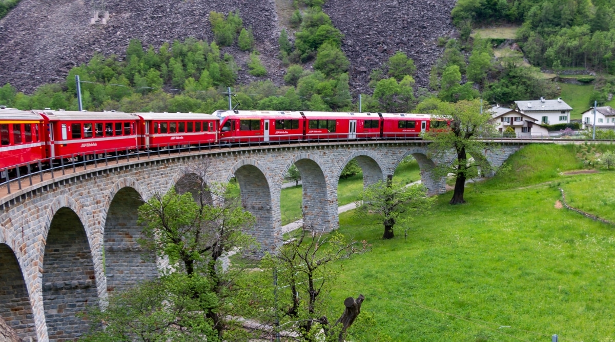 A photograph capturing The Bernina Express traversing the renowned Brusio Spiral Viaduct in Brusio, Switzerland. The image showcases the train navigating the spiral structure, a distinctive engineering feature.