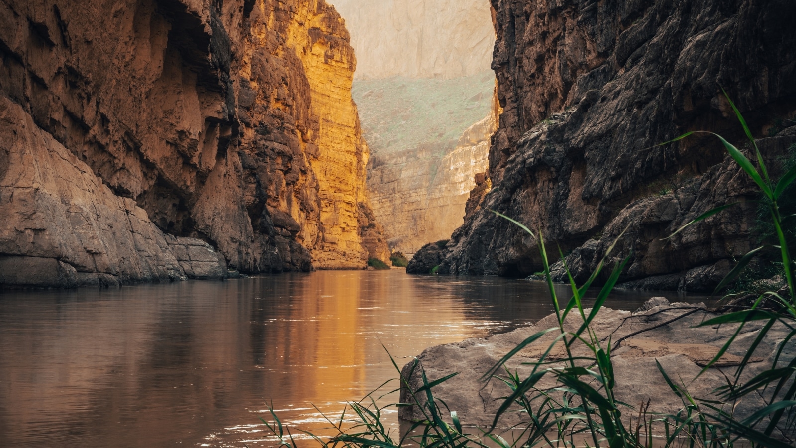 A photograph depicting Big Bend National Park in Texas, USA, with a focus on the Rio Grande and Santa Elena Canyon. The image captures the vast landscape of the park, featuring the river winding through the iconic canyon. The arid terrain, characteristic of the region, extends to the horizon.