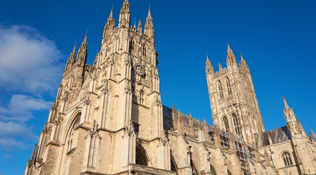 An image capturing Canterbury Cathedral, a historic landmark in Kent, England. The photograph provides a straightforward depiction of the cathedral's exterior architecture, featuring the iconic spires and intricate details. The subdued color palette and clear skies provide an unembellished view of the cathedral against the surrounding urban landscape.