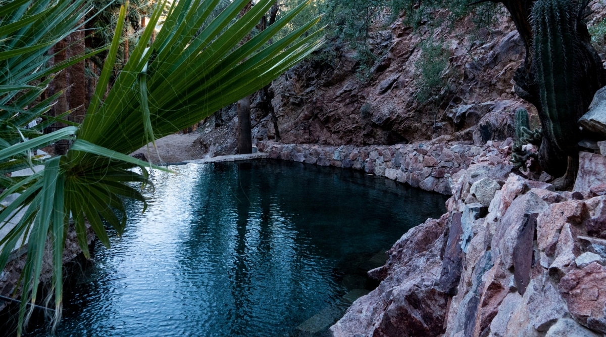 A close-up photograph of Castle Hot Springs, Arizona, framed by rocky terrain and some greenery. The image provides a detailed view of the architectural features of Castle Hot Springs against the surrounding natural landscape.