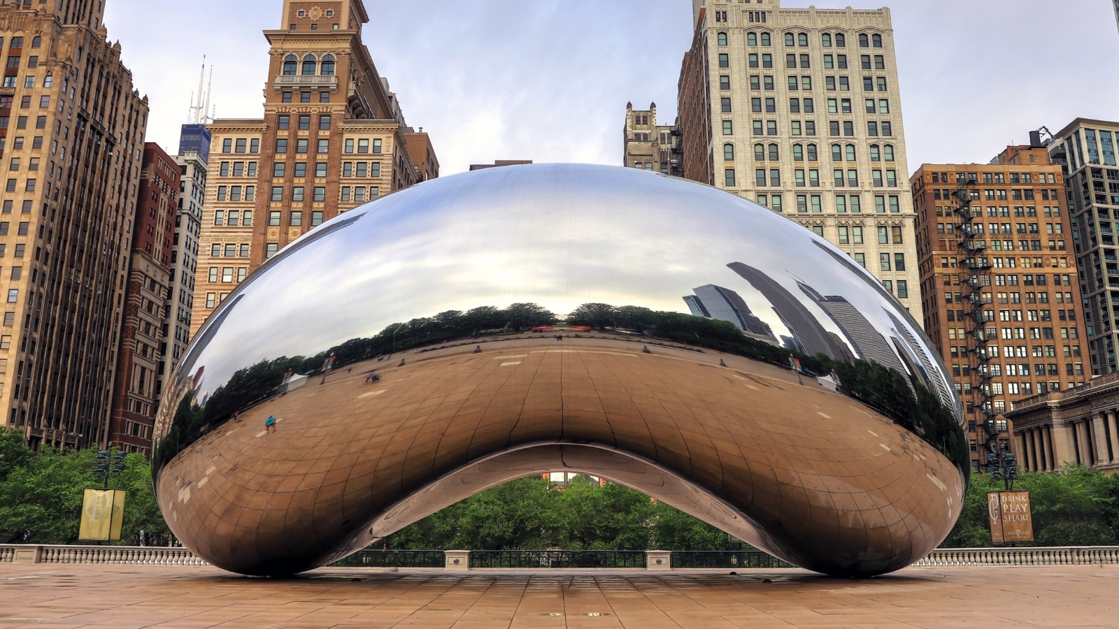A photograph featuring 'Cloud Gate,' also recognized as 'The Bean,' in Millennium Park, Downtown Chicago, Illinois, USA. The image captures the reflective sculpture against the urban backdrop. 'The Bean' is a prominent public artwork known for its polished, mirrored surface and distinctive elliptical shape.
