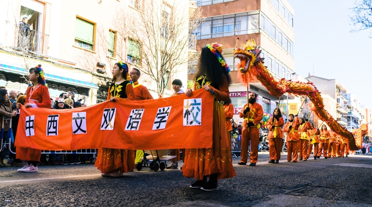 The image captures a Chinese New Year parade in Beijing, featuring individuals predominantly dressed in red and yellow outfits as they walk down the street. Above them, a red and yellow dragon is prominently displayed.