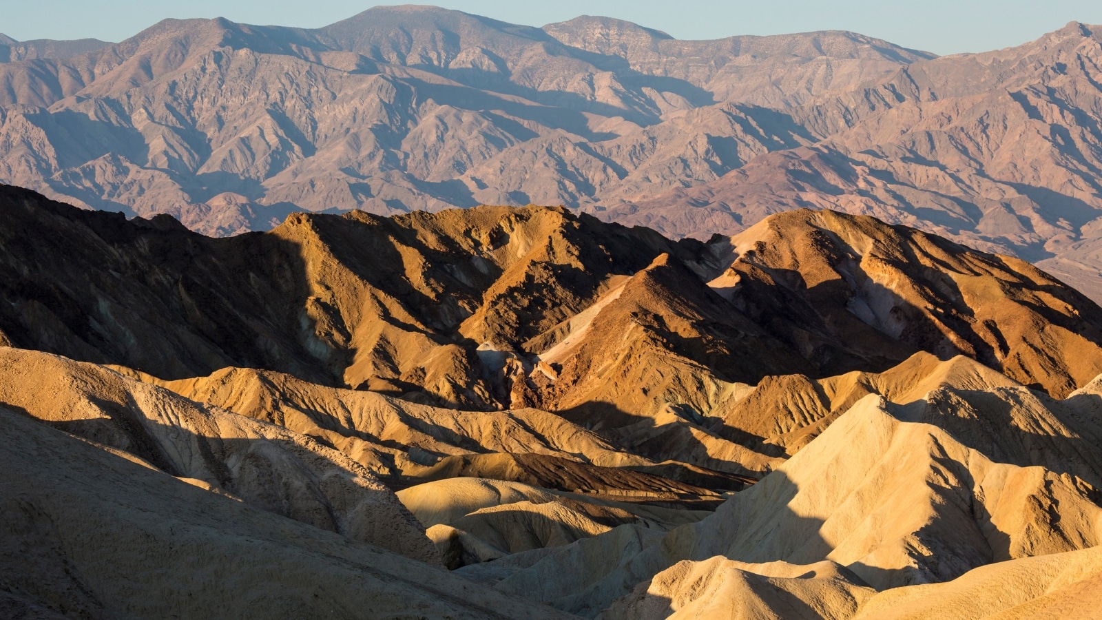 A landscape photograph capturing the morning light at Zabriskie Point in Death Valley National Park, California. The image showcases the natural beauty of the arid terrain and geological formations illuminated by the soft morning light