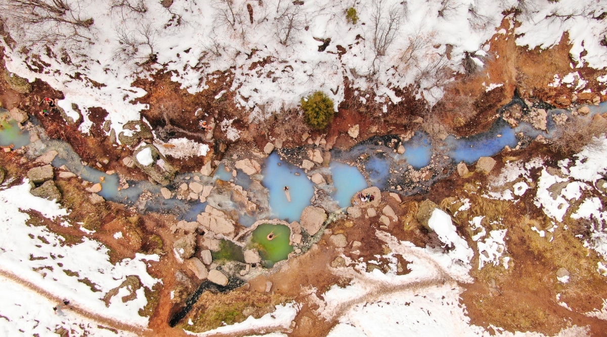 An aerial view capturing Diamond Fork Hot Springs in Utah. The image features the natural hot springs in a scenic outdoor setting surrounded by wilderness. The pools of geothermally heated water are visible, offering a glimpse of the area's natural features. 