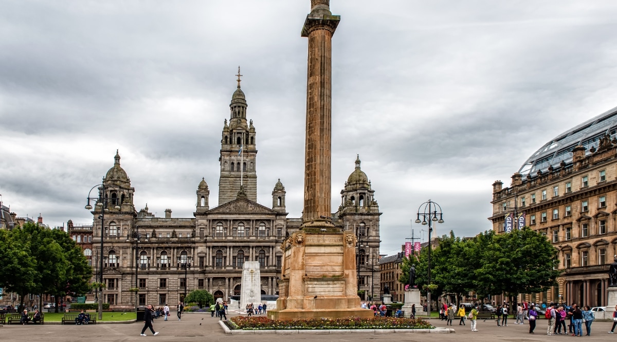 A photograph capturing George Square in the city center of Glasgow, United Kingdom. The image depicts the urban square, surrounded by various architectural structures.