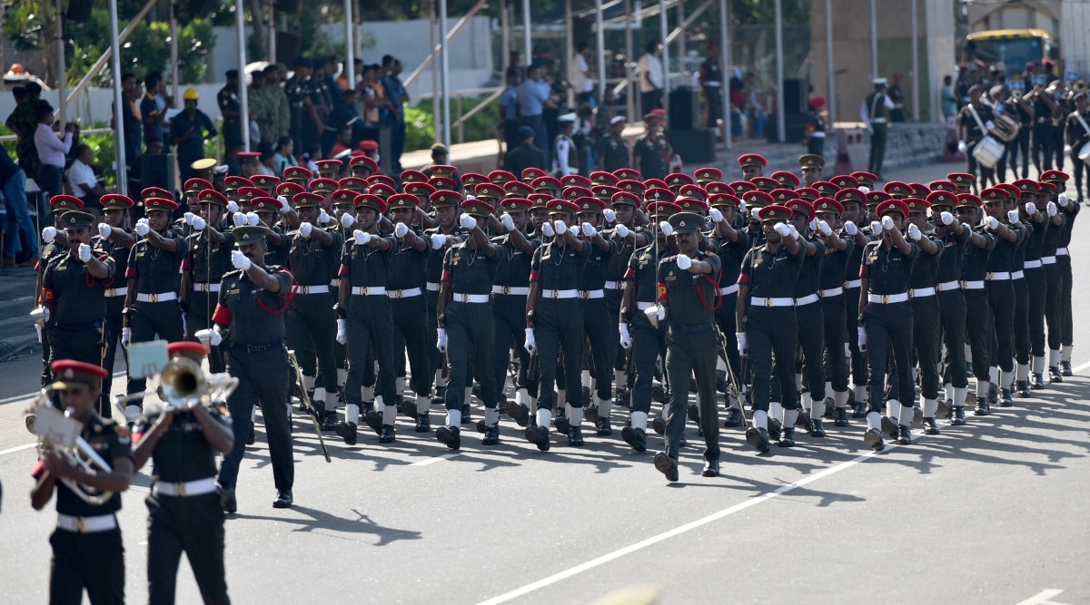 A photograph capturing the Independence Day celebrations in Sri Lanka. The image features a military parade with personnel marching in a column. The participants are clad in military attire, including red headdresses, indicative of a ceremonial display. 