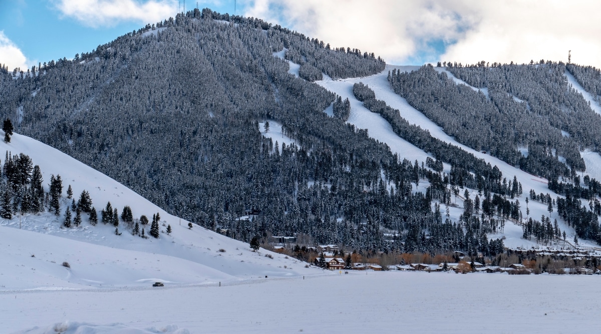  A winter view capturing snow-capped mountains in Jackson, Wyoming. The image features the cityscape nestled beneath the snowy peaks, with residential houses visible against the winter landscape. The mountains exhibit abundant vegetation, primarily fir trees, contributing to the overall wintry scenery.
