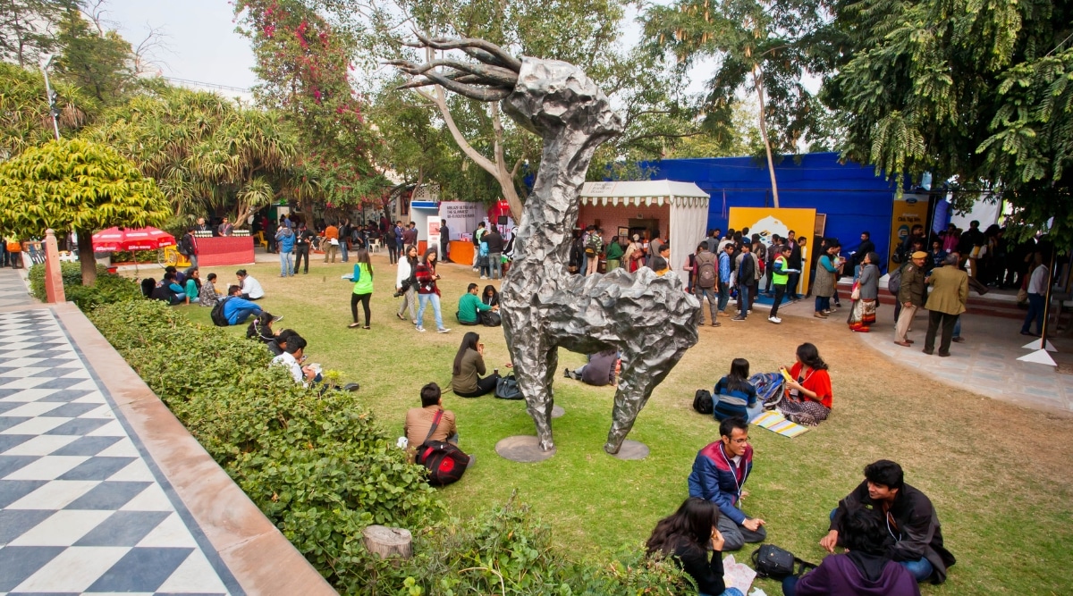 A photograph capturing the scene at the Jaipur Literature Festival. The image features attendees gathered in an outdoor setting, engaging in literary discussions and various activities. 