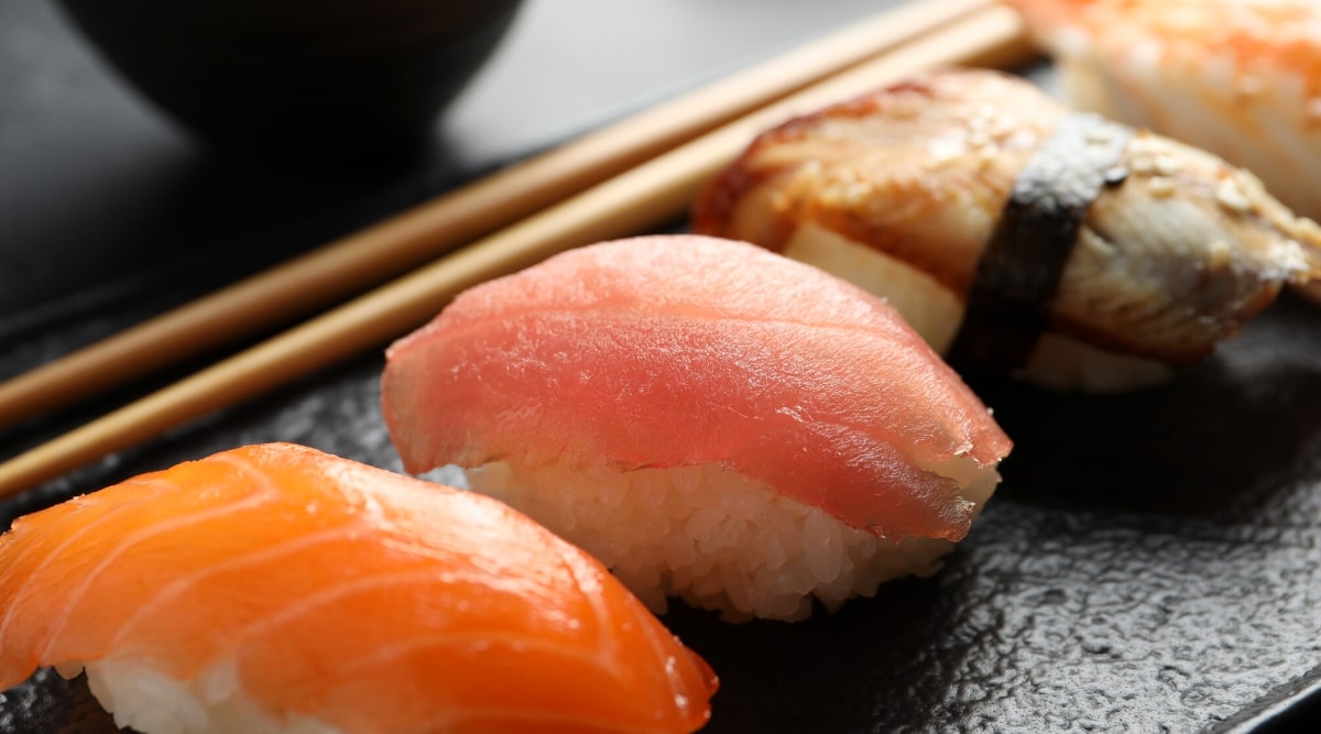 Close-up of a serving board with delicious nigiri sushi and soy sauce on a black table. Each piece consists of expertly crafted vinegared rice, formed into small oblong shapes and topped with a variety of fresh fish including salmon, tuna and eel.