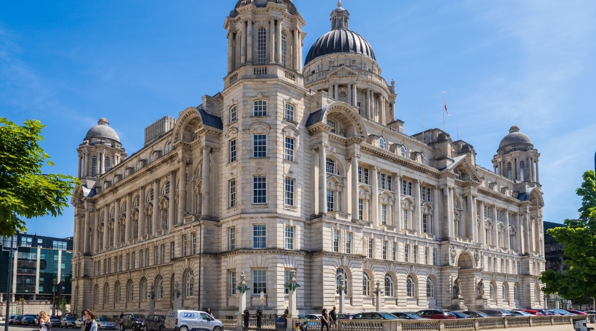 An image capturing Liverpool's waterfront with a focus on the iconic Three Graces. The structures stand prominently against the skyline, serving as significant landmarks. The architecture appears to be well-maintained, and the surrounding waterfront suggests a vibrant urban environment.