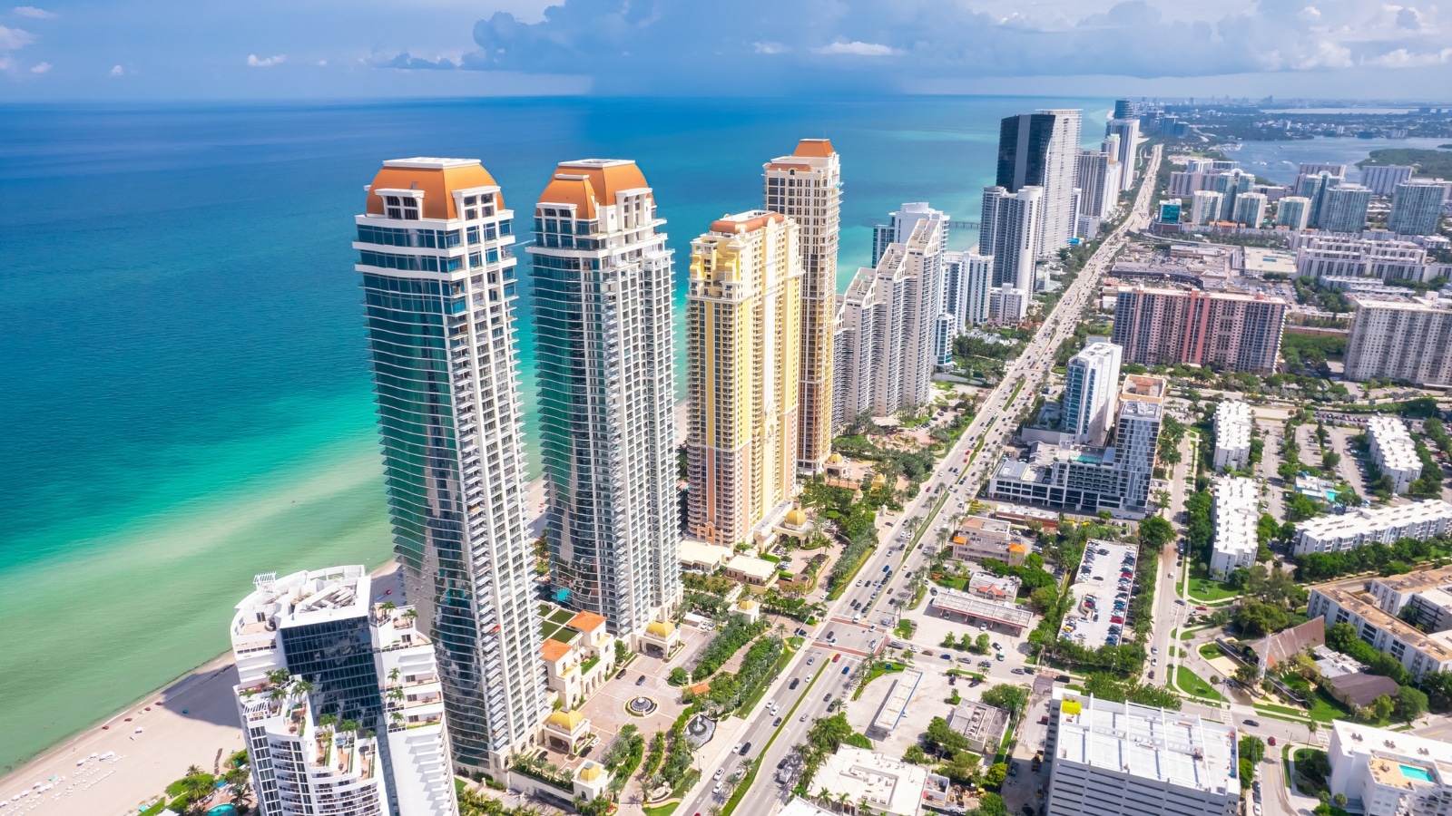 A panorama capturing Sunny Isles Beach in Florida, specifically Miami Beach. The image showcases the Atlantic Ocean beach with a broad seascape. The turquoise color of the sea water is prominently featured, providing a serene and picturesque view.