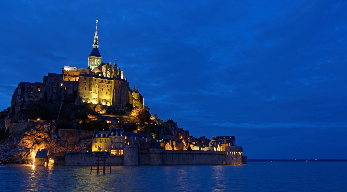 Mont Saint Michel monastery lit up at night during high tide as the lights shimmer on the water.