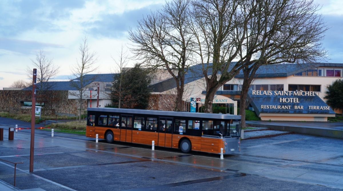A shuttle bus for Mont Saint Michel parked outside the Relais Saint-Michel Hotel in France on a cloudy day.