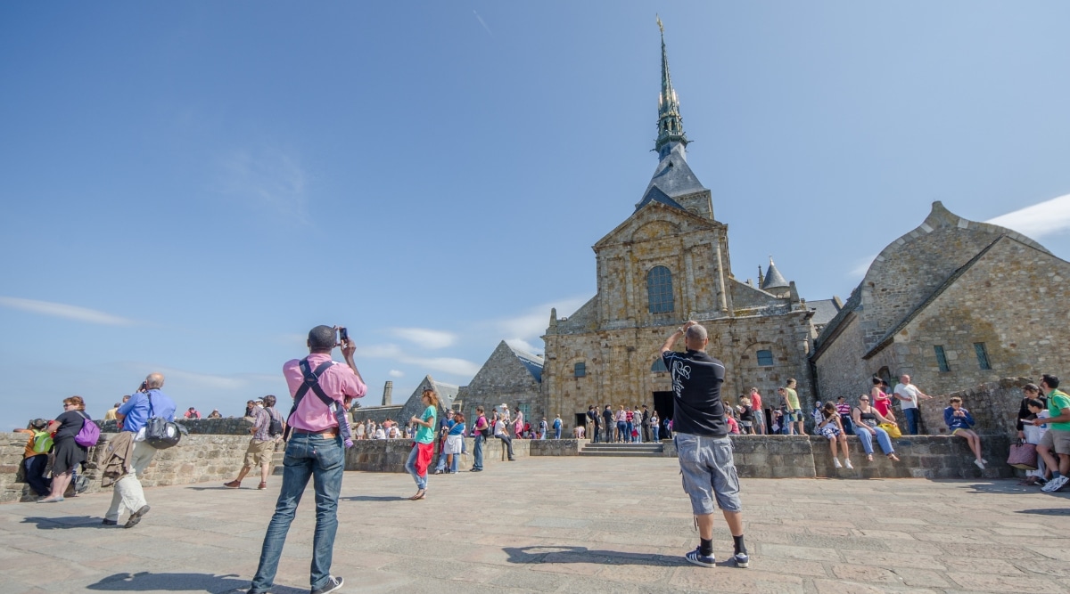 Mont Saint Michel full of tourists taking photos and exploring on a bright sunny day in France.