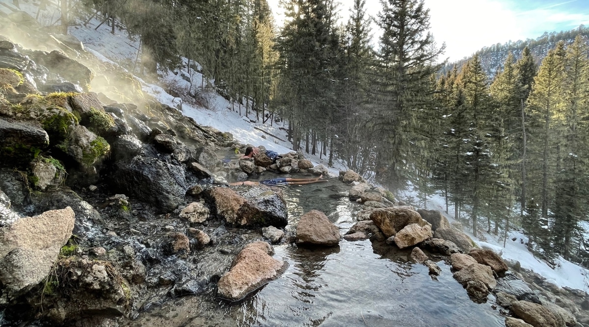 A view capturing San Antonio Hot Springs in New Mexico. The image features a natural spring formed on a mountainside, set against a backdrop of surrounding forest.