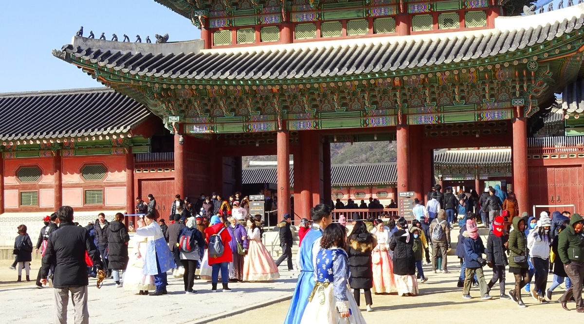 A photograph capturing people in front of Gyeongbokgung Palace. The image depicts a crowd of individuals, suggesting visitor activity in the vicinity of the historical landmark.