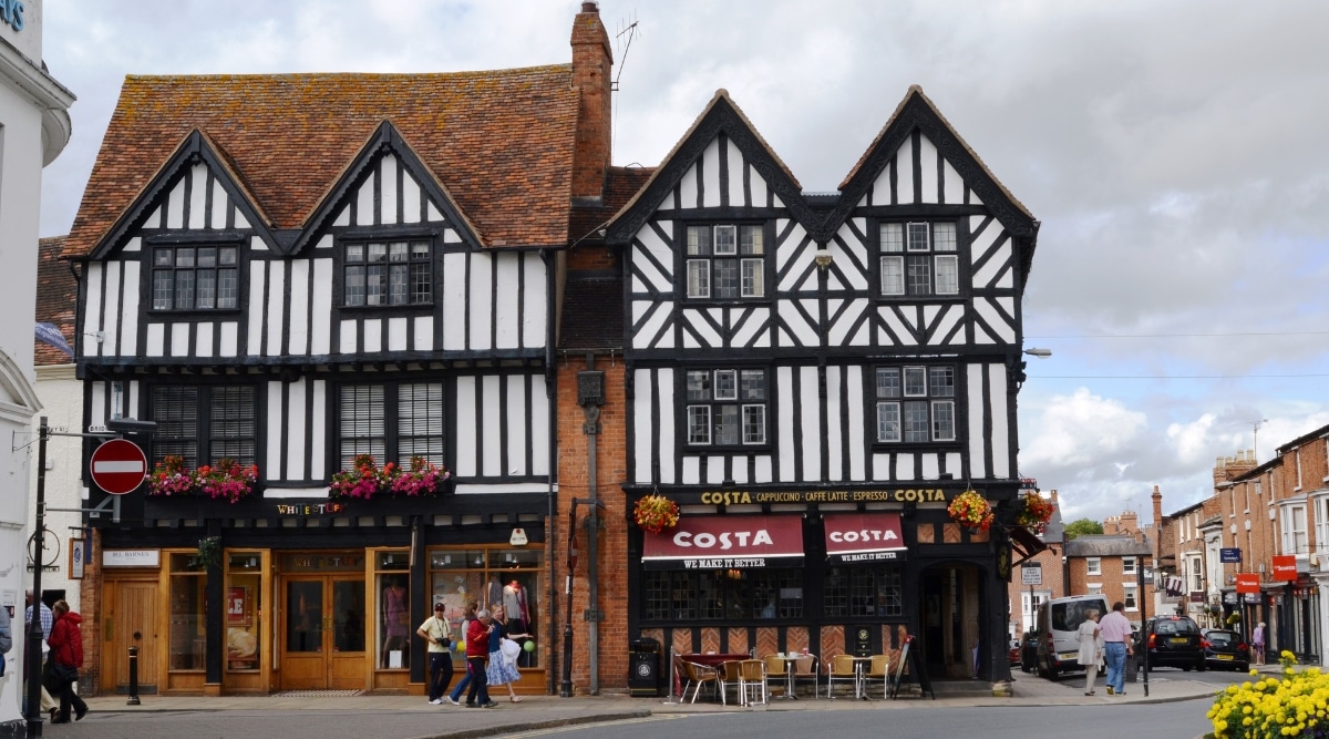 A photograph capturing the historic town of Stratford-upon-Avon, characterized by Tudor-style buildings that contribute to its Shakespearian ambiance. The image showcases the architectural elements of the buildings, reflecting the traditional design prevalent in the region.