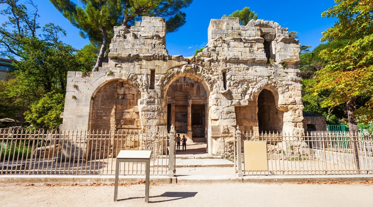 An image capturing Temple de Diane in Nimes, France. The photograph showcases the ancient Roman temple, known for its historical and architectural significance. The weather appears clear, with sunlight illuminating the stone structure. The temple's classic Roman design features well-preserved columns and architectural details.