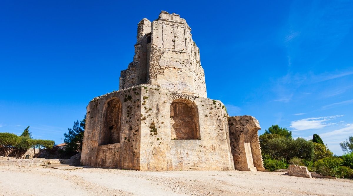 A straightforward photograph capturing Tour Magne in Nimes. The image provides a clear view of the ancient Roman tower, known as Tour Magne, against a neutral sky. The tower stands prominently as part of the historical architecture in Nimes. Its stone structure and surrounding landscape contribute to its historical significance.