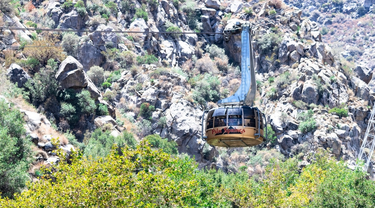 The image captures the Palm Springs Aerial Tramway in motion, traversing Chino Canyon in the San Jacinto Mountains, Palm Springs, California, USA. The tramway features a cable car system with the surrounding landscape of the canyon and mountainous terrain.