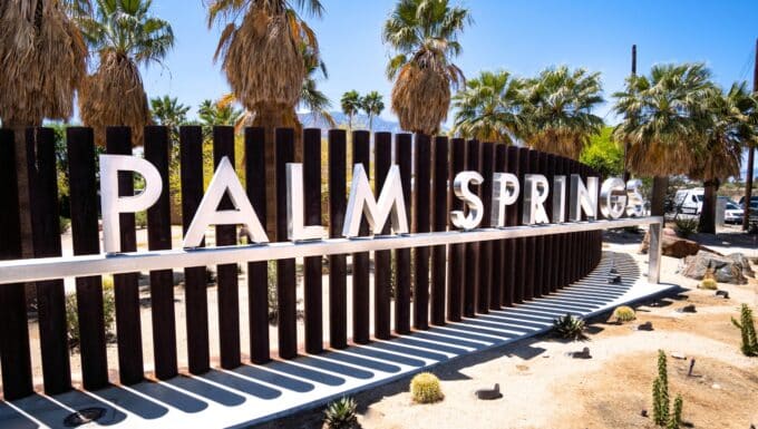 A view capturing a city stele in Palm Springs, with metal letters affixed to a metal stand against a background of wooden slats. The inscription 
