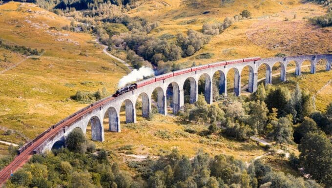 An extensive view capturing a steam train traversing Glenfinnan Viaduct in Scotland. The image showcases the viaduct