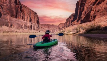 Adventurous Woman on a Kayak paddling in Colorado River. Glen Canyon, Arizona, United States of America. Sunrise Sky Art Render. American Mountain Nature Landscape Background.