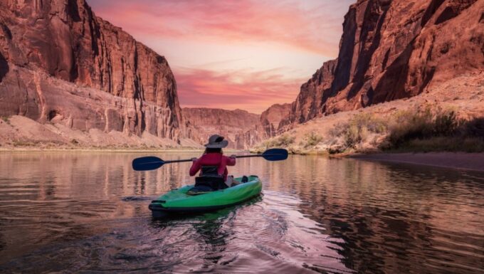 Adventurous Woman on a Kayak paddling in Colorado River. Glen Canyon, Arizona, United States of America. Sunrise Sky Art Render. American Mountain Nature Landscape Background.