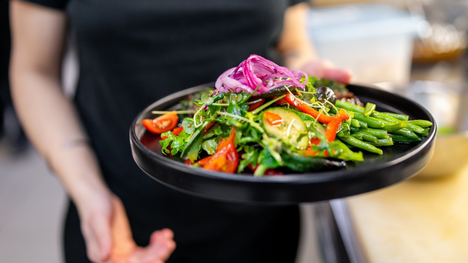 An image depicting an individual holding a vibrant salad plate. The plate contains fresh green beans, red tomatoes, and purple onions.