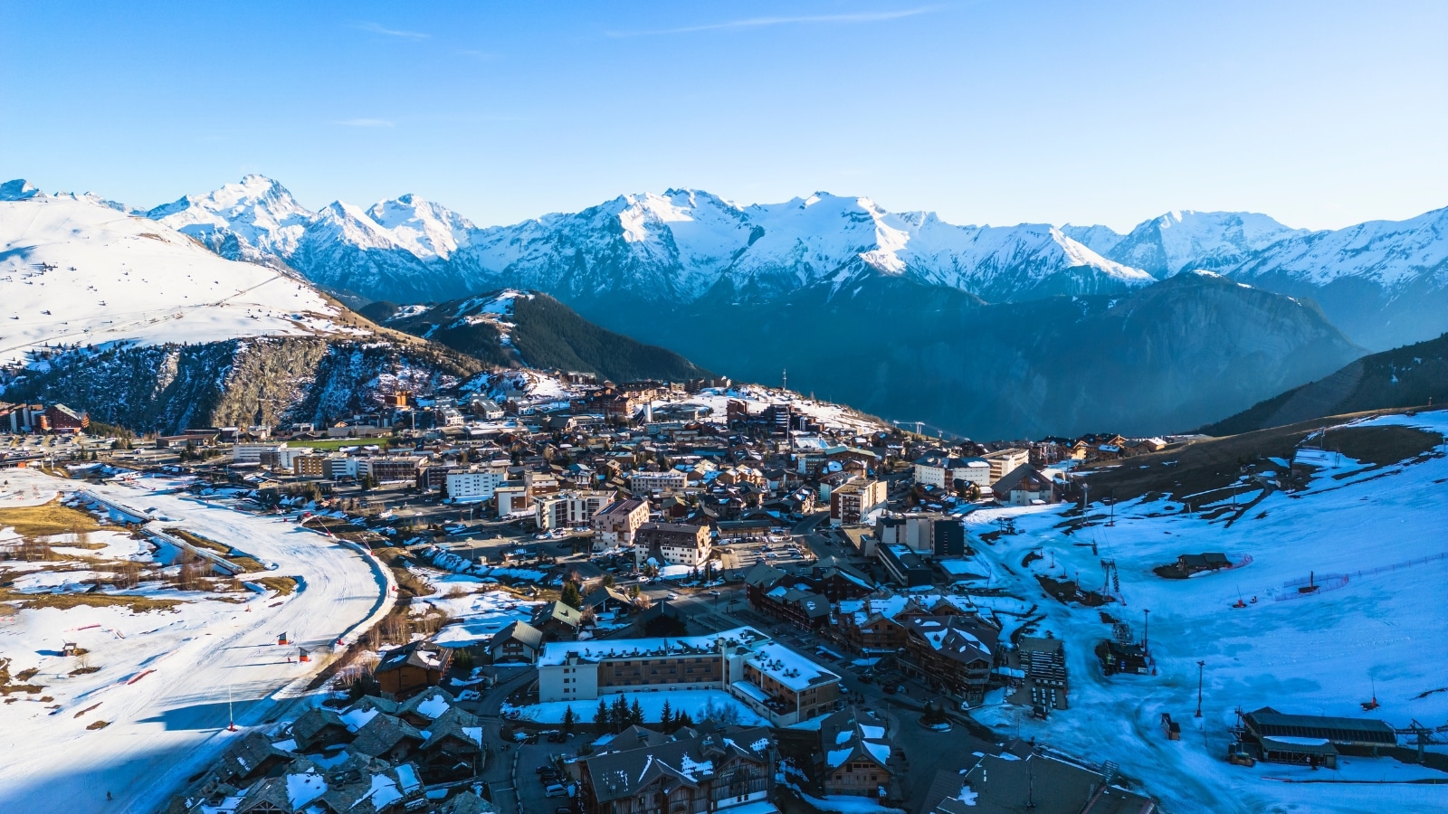 The photograph captures a town in the foreground against the backdrop of the Alpe d'Huez mountains in France. The town's features are discernible, exhibiting typical urban structures. The mountains, visible in the background, present a scenic panorama.