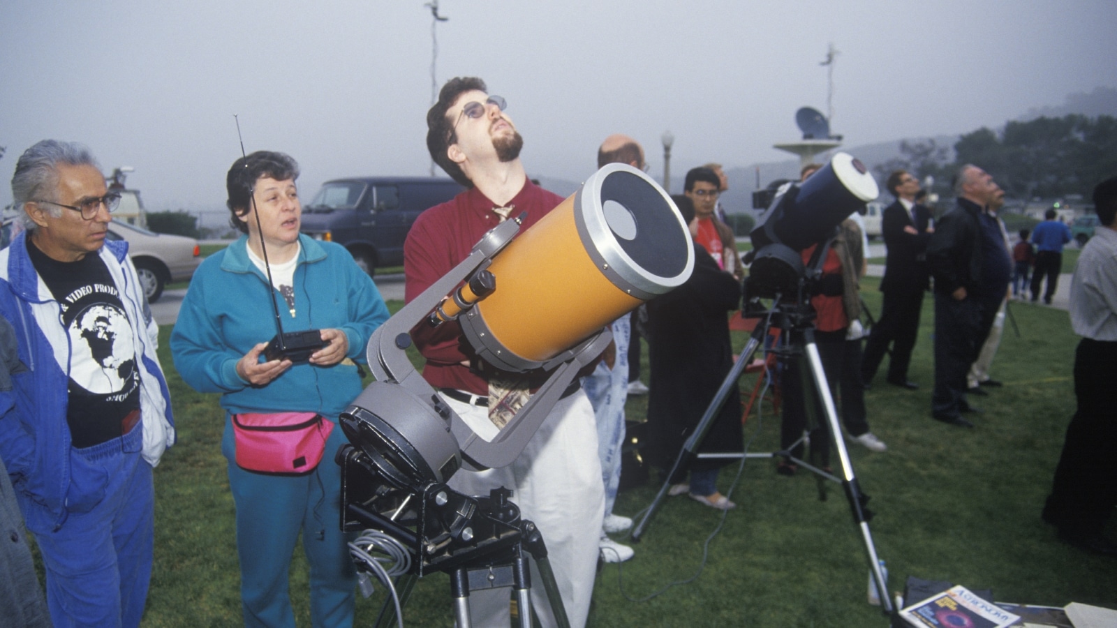 The image depicts amateur astronomers observing a solar eclipse. They are using specialized equipment like telescopes and solar filters to safely view the phenomenon.