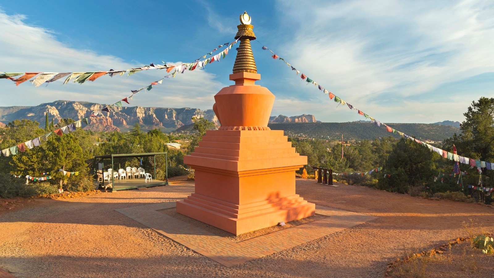 A photograph capturing Amitabha Stupa and Prayer Flags in Peace Park, Sedona Arizona. The image showcases the stupa's architectural structure amidst a serene natural landscape featuring distant red rock formations. Prayer flags flutter in the breeze, adding a colorful touch to the scene.