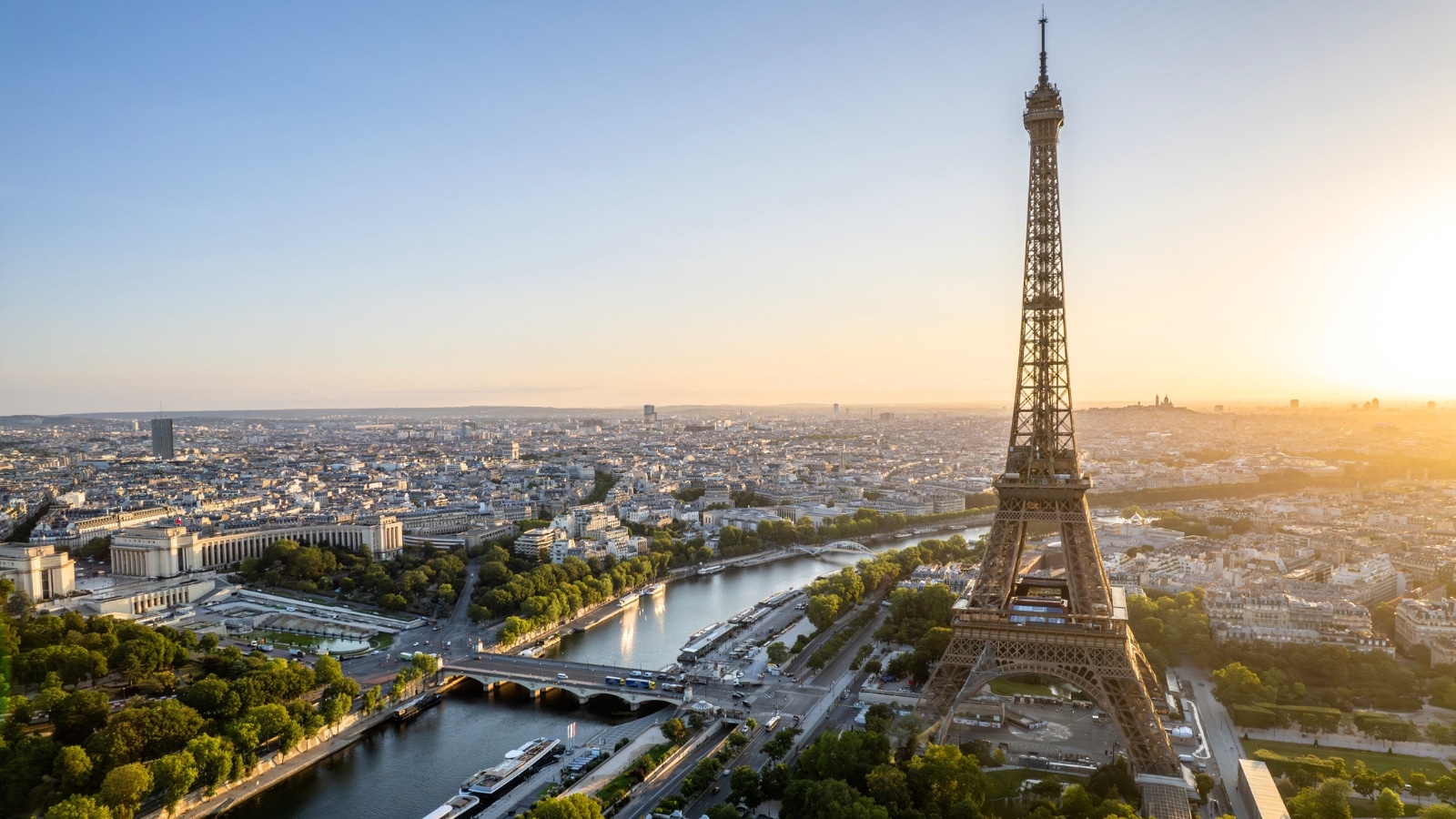 An aerial view showcasing the streets of Paris, France, with the iconic Eiffel Tower in the background during sunset. The image captures the city's urban layout, with streets and buildings visible beneath a colorful sunset sky. The Eiffel Tower stands prominently, recognizable against the Parisian skyline.