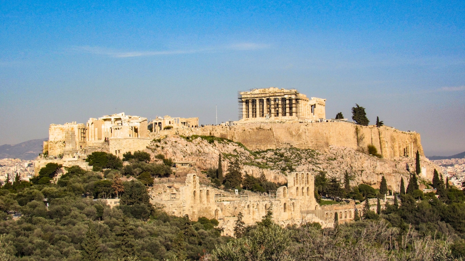 A photograph depicting The Parthenon Temple against a sunny summer day with a clear blue sky. The image showcases the architectural features of The Parthenon, an iconic structure atop the Acropolis mountain in Athens, Europe.