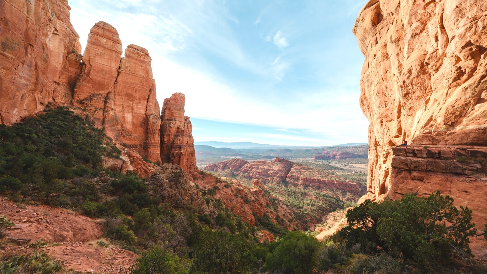 A view from the top of Cathedral Rock Trail in Sedona, Arizona. The image captures the scenic viewpoint at the summit, showcasing the rugged terrain and red rock formations characteristic of the area. The viewpoint offers a panoramic perspective of the surrounding landscape, with sparse vegetation dotting the rocky terrain.