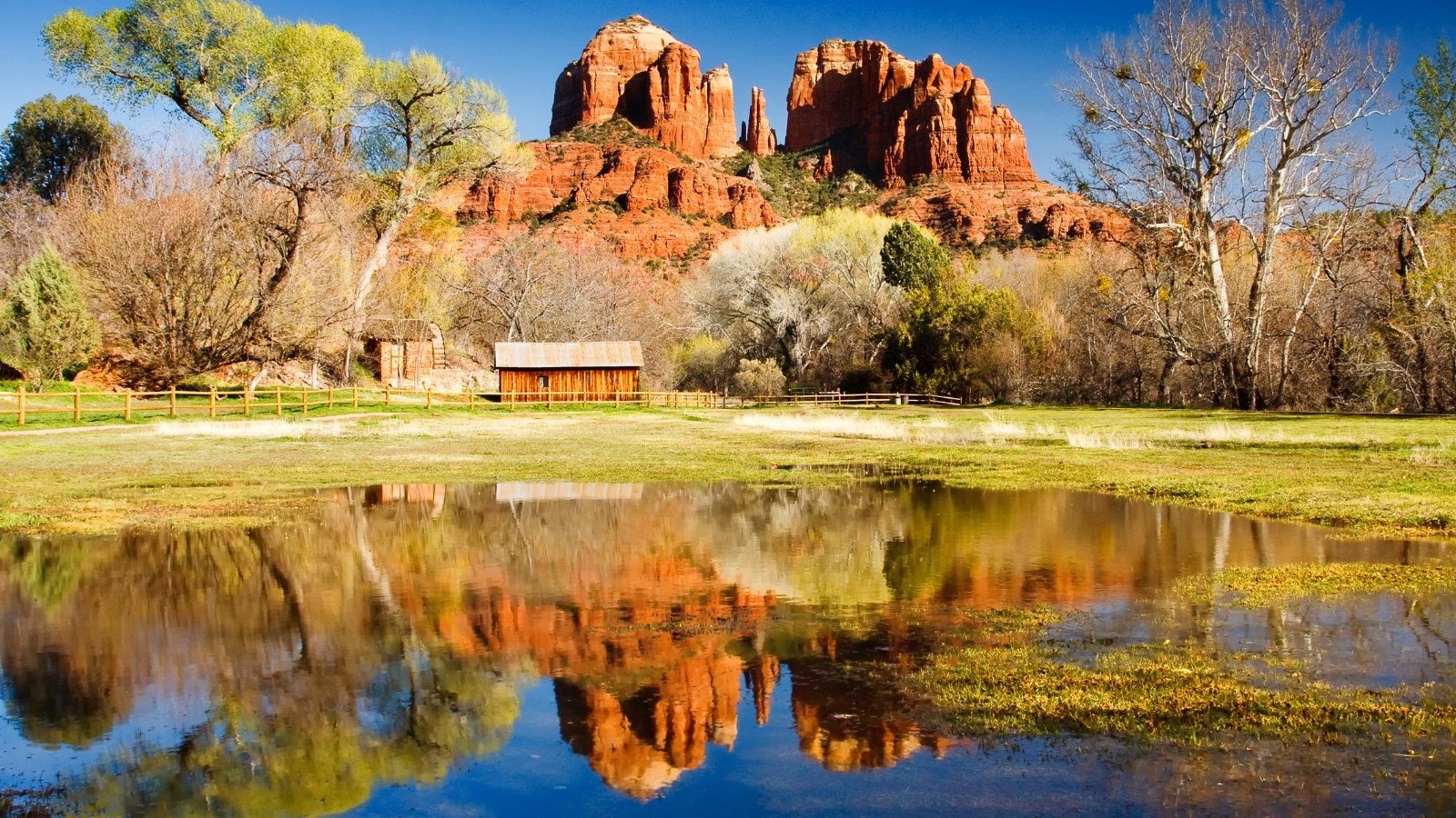 The view of Cathedral Rock in Sedona, Arizona. The towering rock formations stand out like beacons in the dimmed landscape of the Red Rock State Park. In the distance there is an old wooden barn.