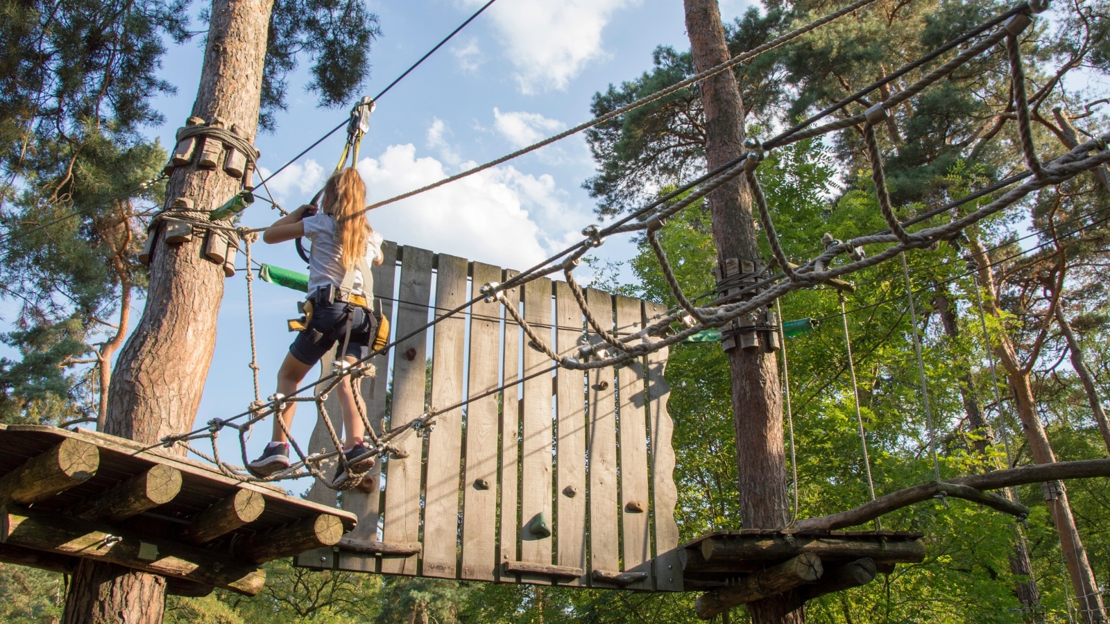 The photograph captures a girl engaged in rope climbing activities within a rope park, surrounded by abundant greenery.