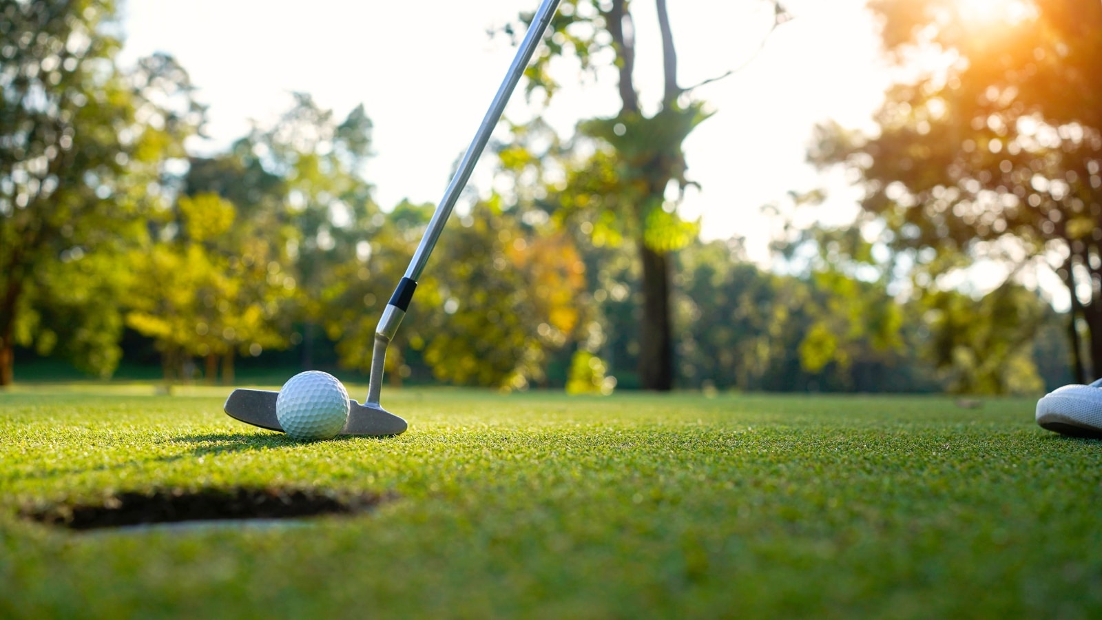 A close-up photograph featuring a golf club and golf ball positioned on a grassy surface.