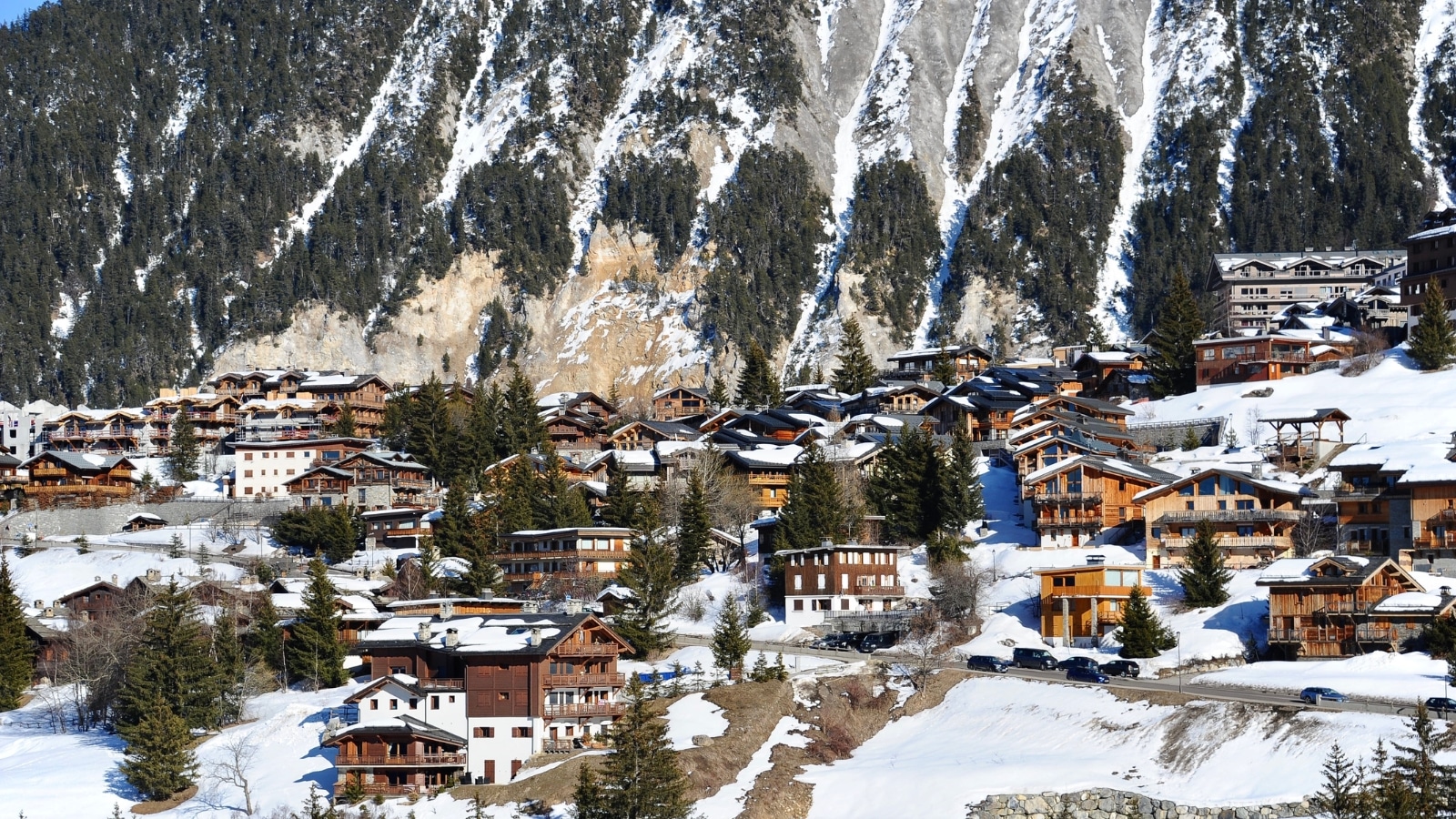 The image features the town's architecture with prominent wooden chalets set against a snow-covered landscape. The visual showcases the seasonal ambiance.