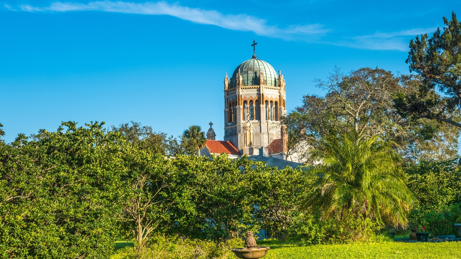 The image shows the top of Memorial Presbyterian Church (1889) in St. Augustine, Florida, United States, with a green landscape below. The church's architecture is prominent, featuring intricate details and a distinct roofline.