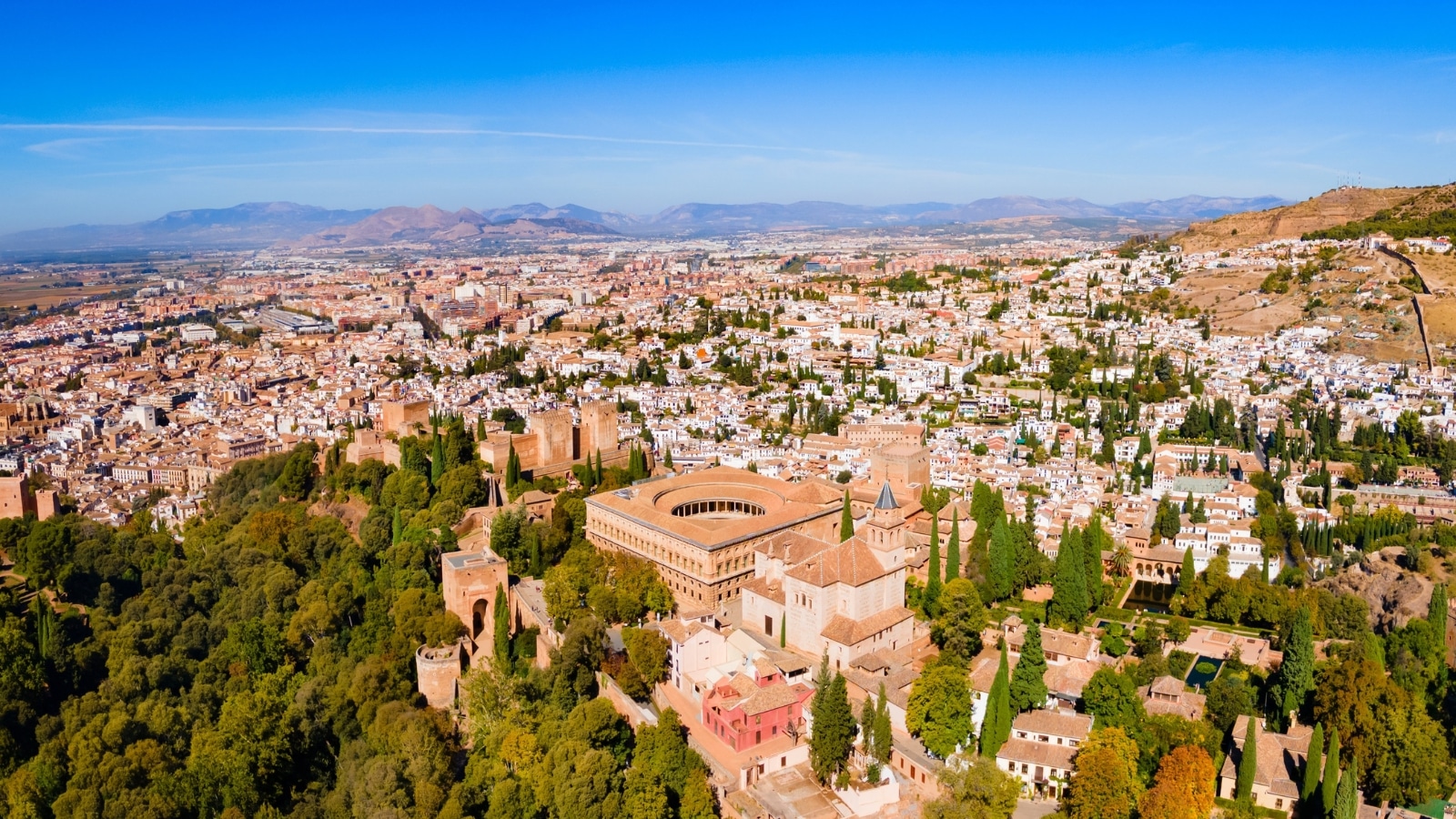 An aerial panoramic view capturing The Alhambra, a fortress complex situated in Granada, Andalusia, Spain. The image offers a comprehensive perspective of the architectural layout of The Alhambra against the surrounding landscape.
