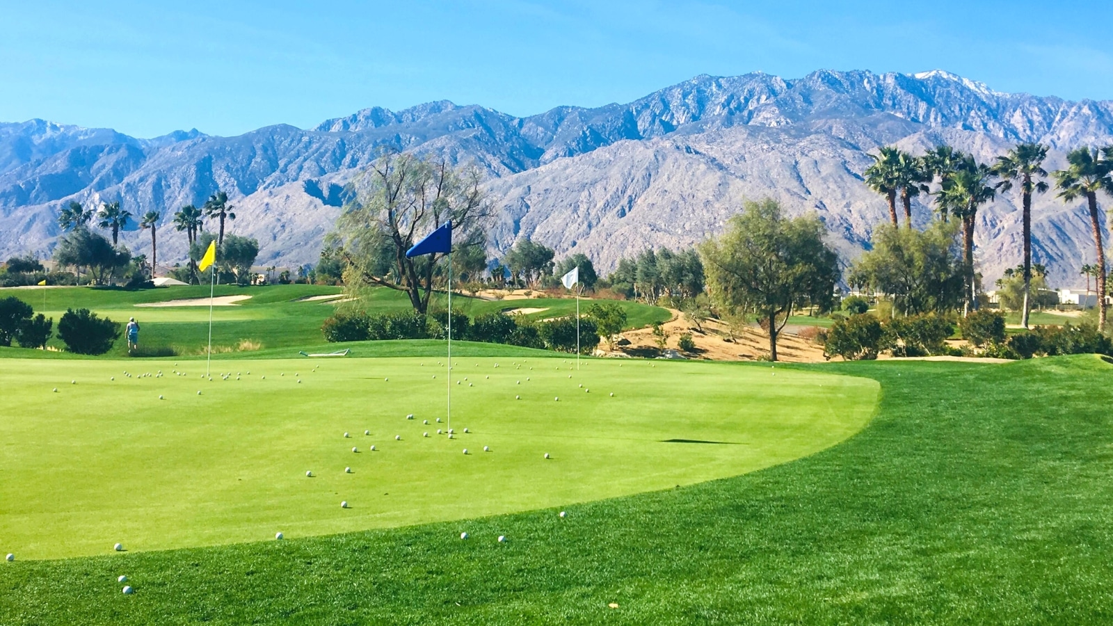 An image capturing the golf course at Indian Canyon Golf Resorts in Palm Springs. The photograph features a well-maintained golf course with lush greenery, framed by a backdrop of distant mountains under a clear sky.