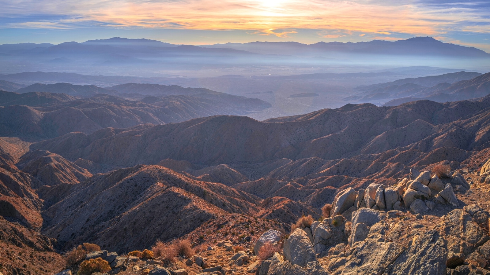 A photograph capturing the landscape from Keys View summit in Joshua Tree National Park, Southern California, USA. The image showcases the expansive vista at sunset, featuring mesas, Coachella Valley.