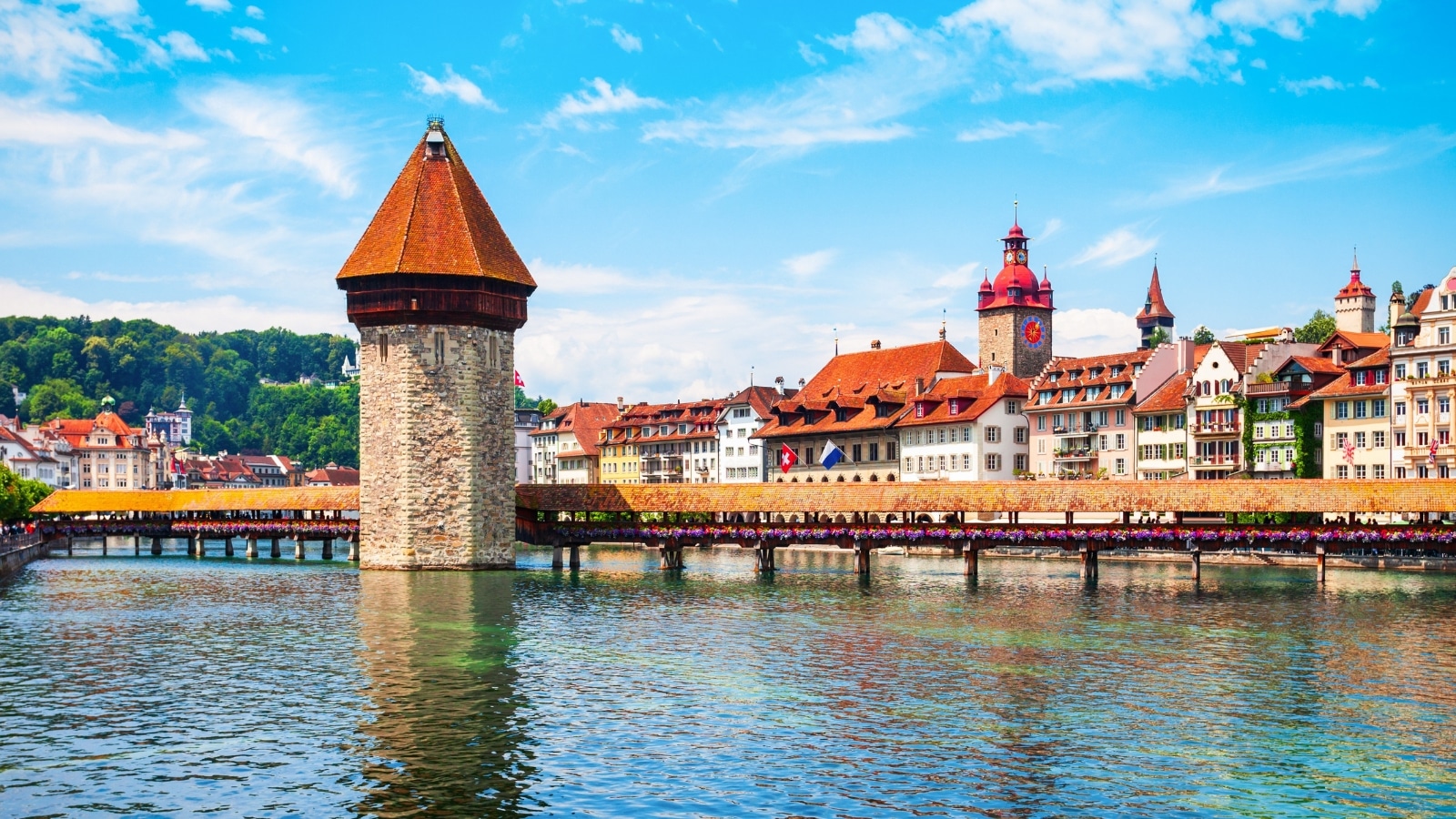 A photograph capturing Kapellbrucke, also known as Chapel Bridge, in Lucerne. The wooden footbridge spans the Reuss River and leads towards the Wasserturm water tower.