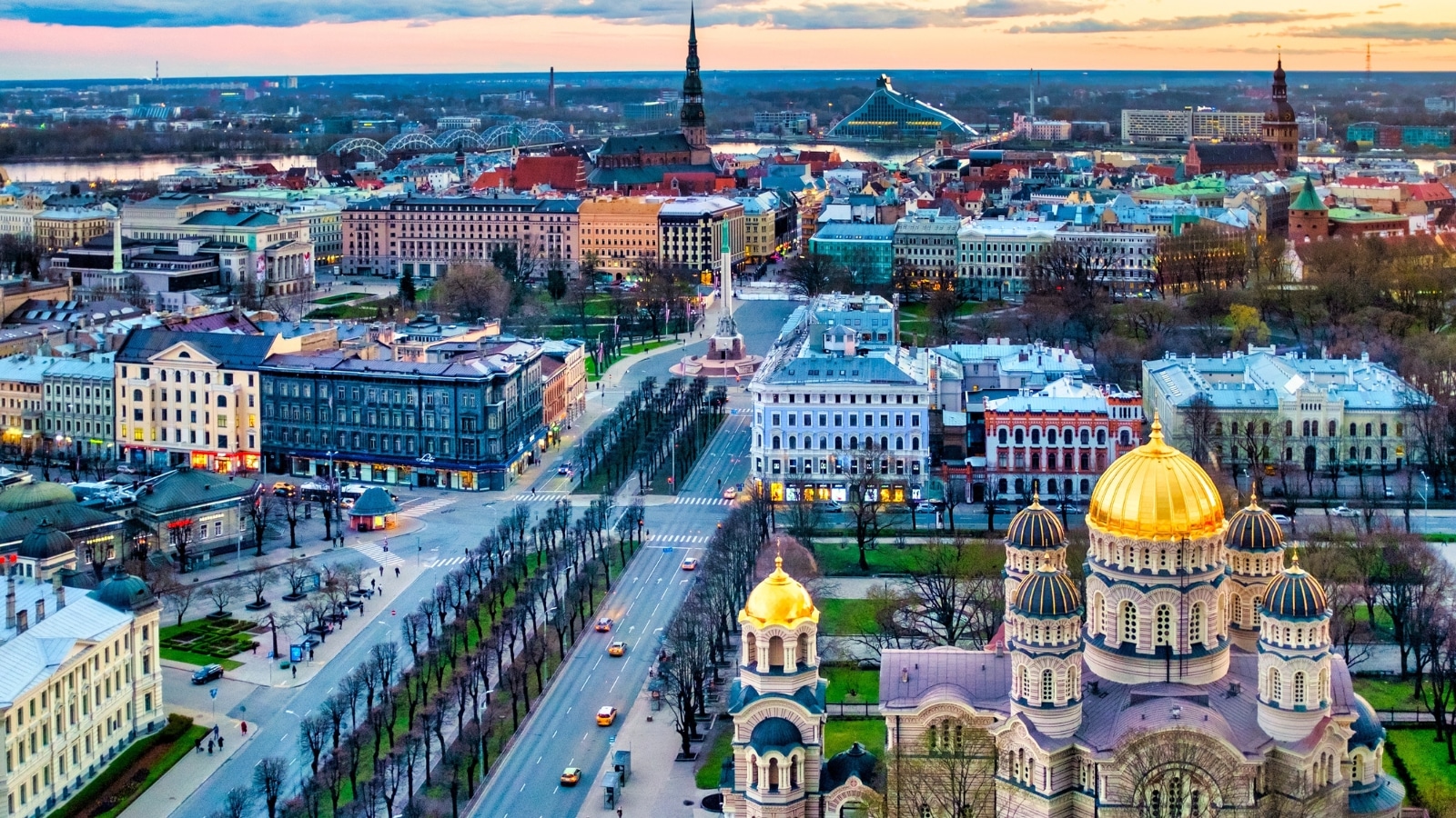 A panoramic view of the city of Riga, Latvia. The image captures the urban landscape featuring notable architectural structures and the city skyline. The photograph showcases a mix of residential and commercial buildings, along with green spaces.