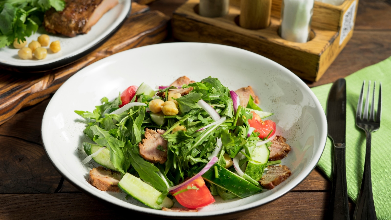 A photograph displaying a salad composition featuring ham, arugula, and assorted vegetables served on a white plate.