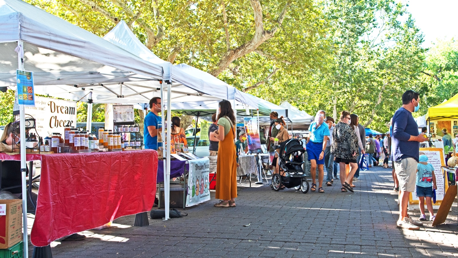 A photograph depicting the Sedona Farmers Market in Sedona, Arizona. The image captures a scene of vendors' stalls, showcasing fresh produce and goods. Visitors can be seen browsing the market, suggesting a typical day of shopping and browsing.