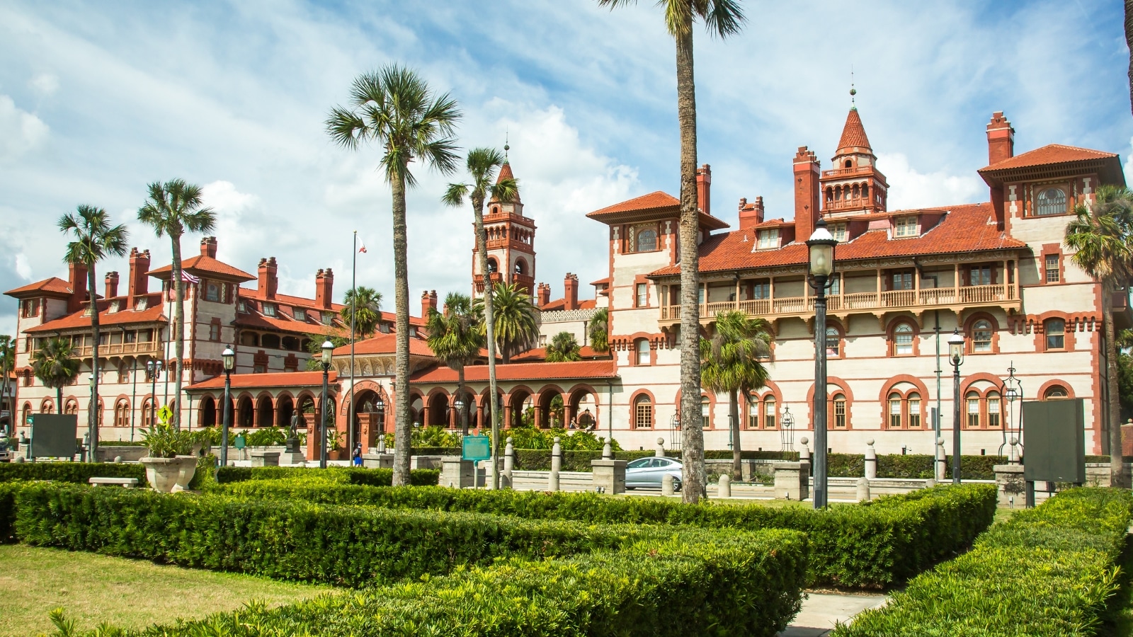 The image shows Flagler College in St. Augustine, Florida, displaying the architectural features of the historic building. The college's distinctive Spanish Renaissance Revival style is prominent, characterized by ornate details and red-tiled roofs.