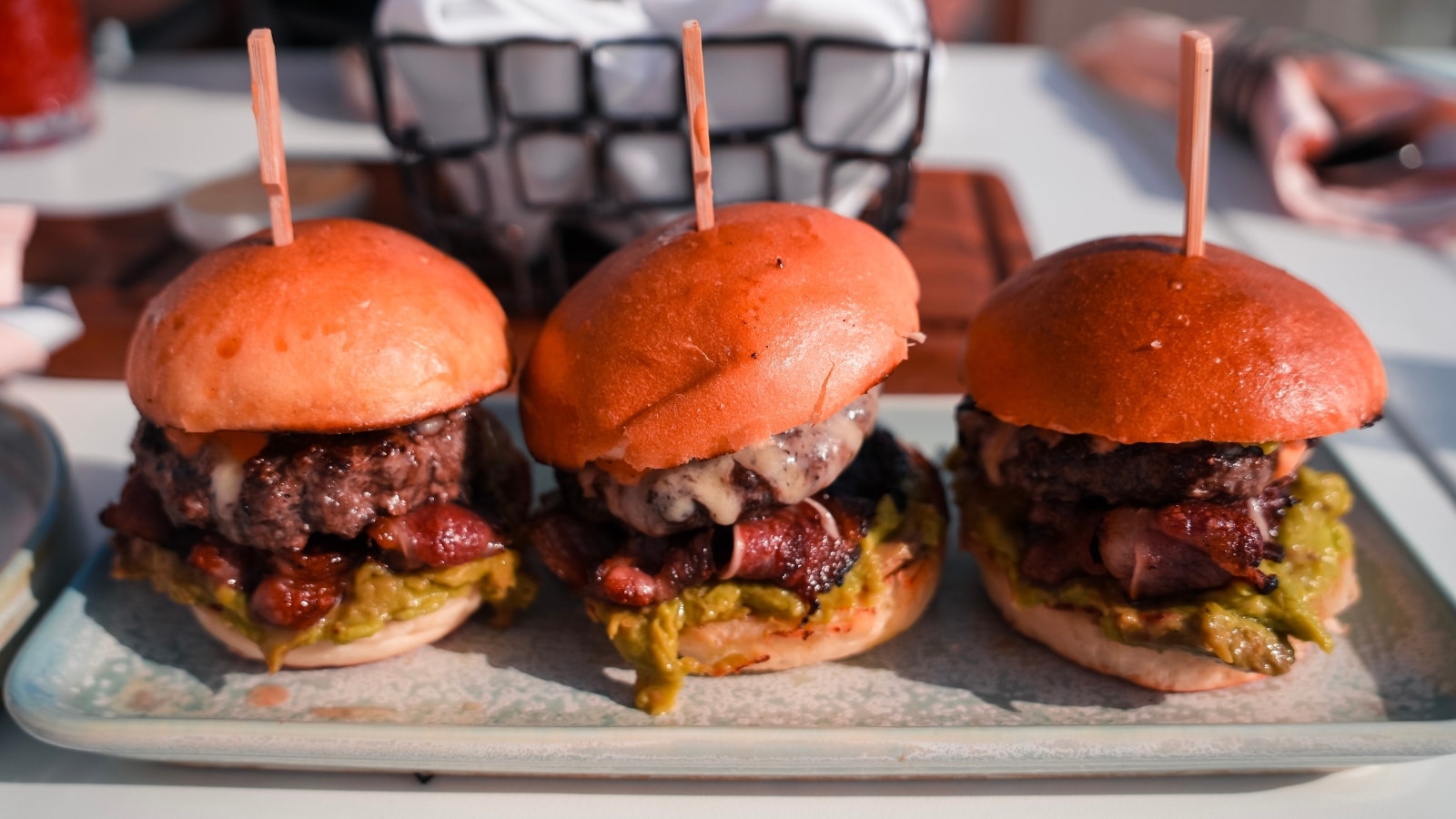 The image features a close-up view of three mini-burgers neatly arranged on a plate, each skewered for presentation.
